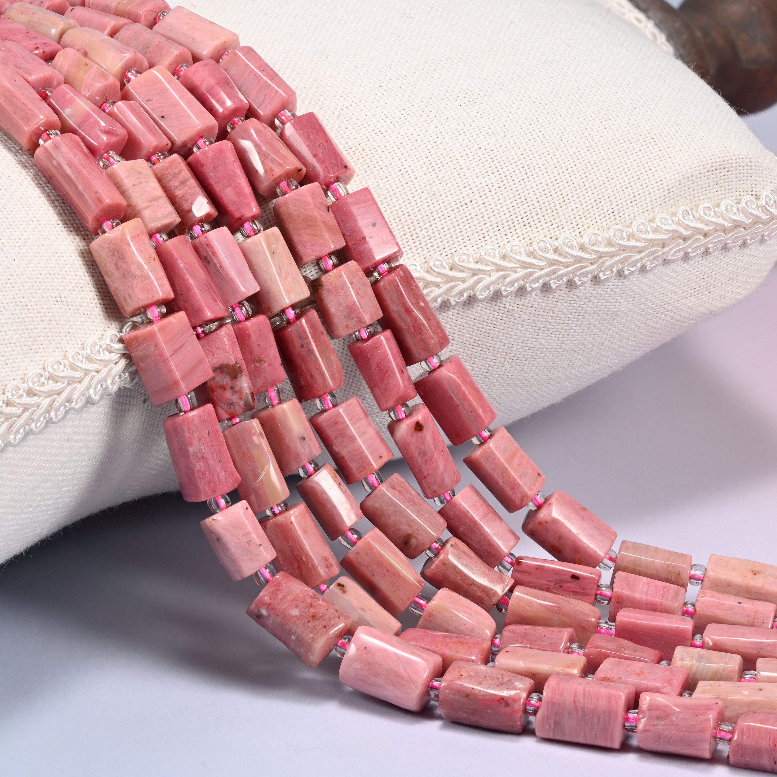 Pink Rhodonite faceted tube beads draped in rows, dusty rose tubes streaked with cream and beige, spaced with small pink glass seed beads