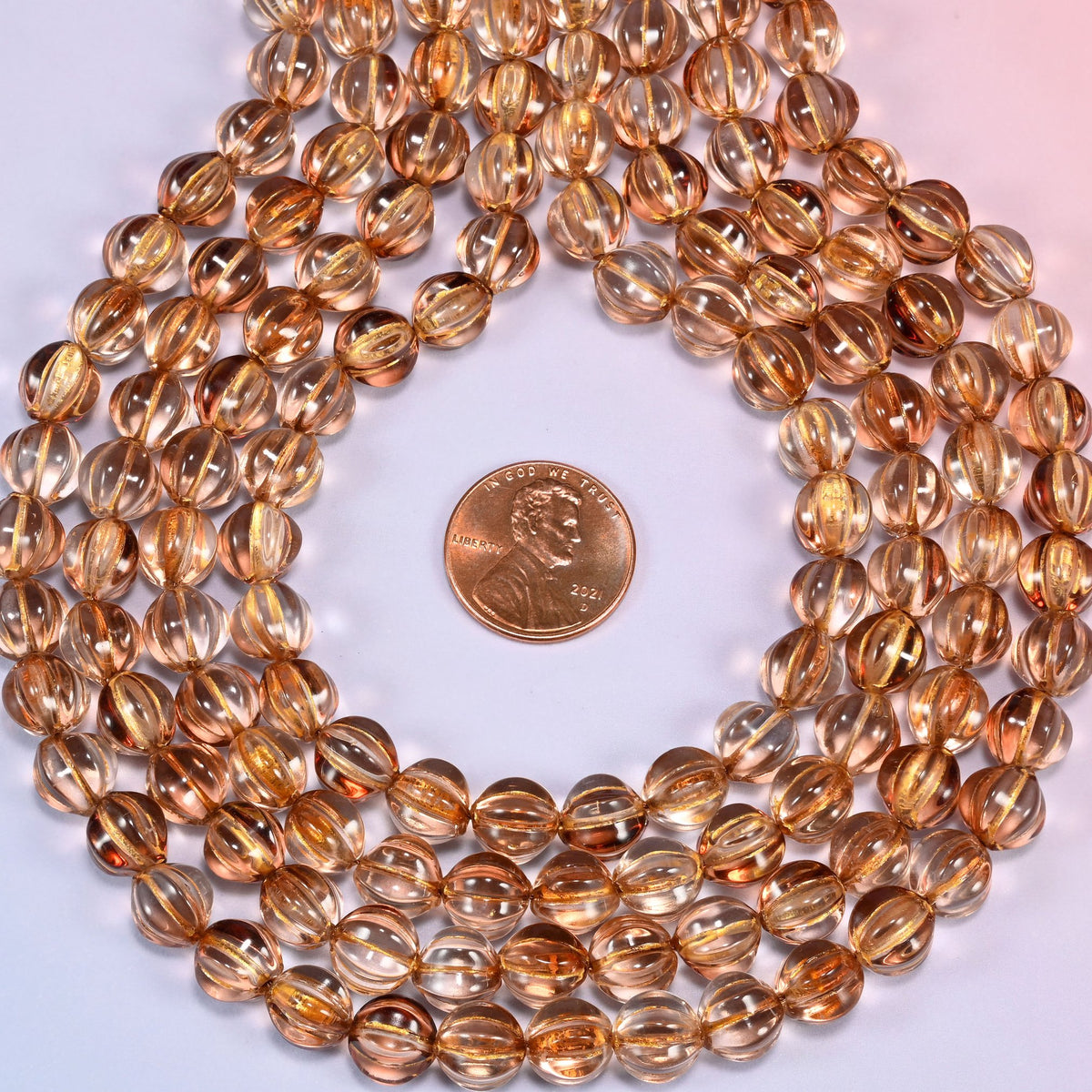 Brown pumpkin glass beads coiled into a ring, shown with a US penny in the open center for scale.