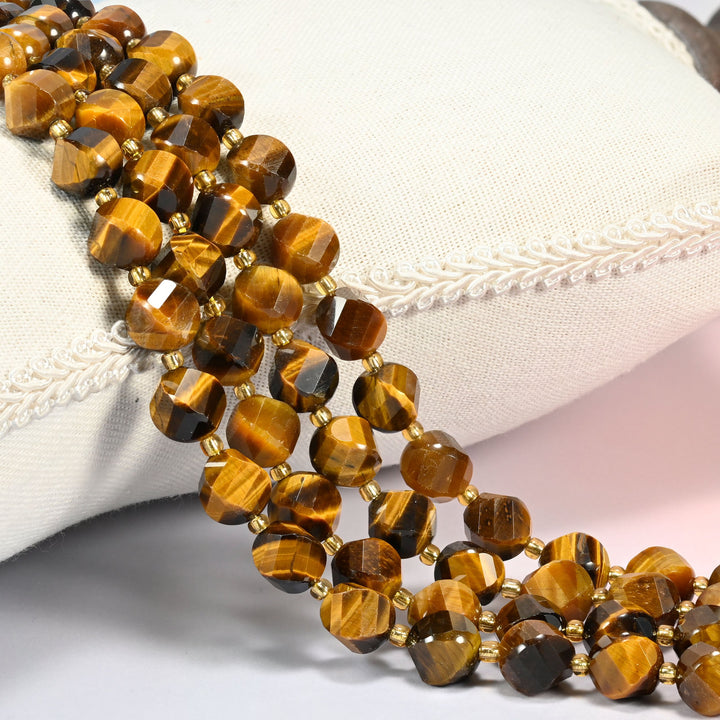 A+ tiger eye faceted spiral twist beads 10mm with small gold spacer beads, several strands draped over a white cushion