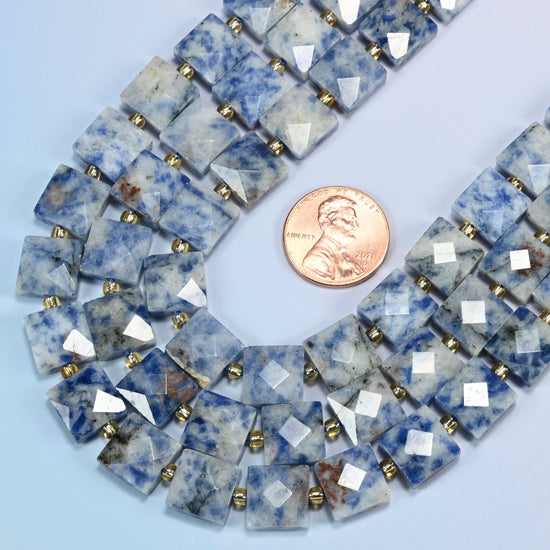 Close view of natural blue spot jasper faceted flat square strands curving beside a US penny for scale