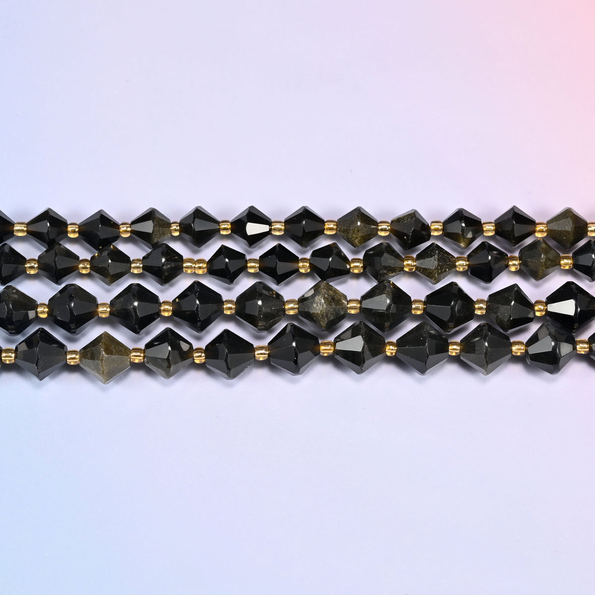Gold obsidian bicone beads in straight rows, seen close up, each bead cut to two points meeting at a wide center.