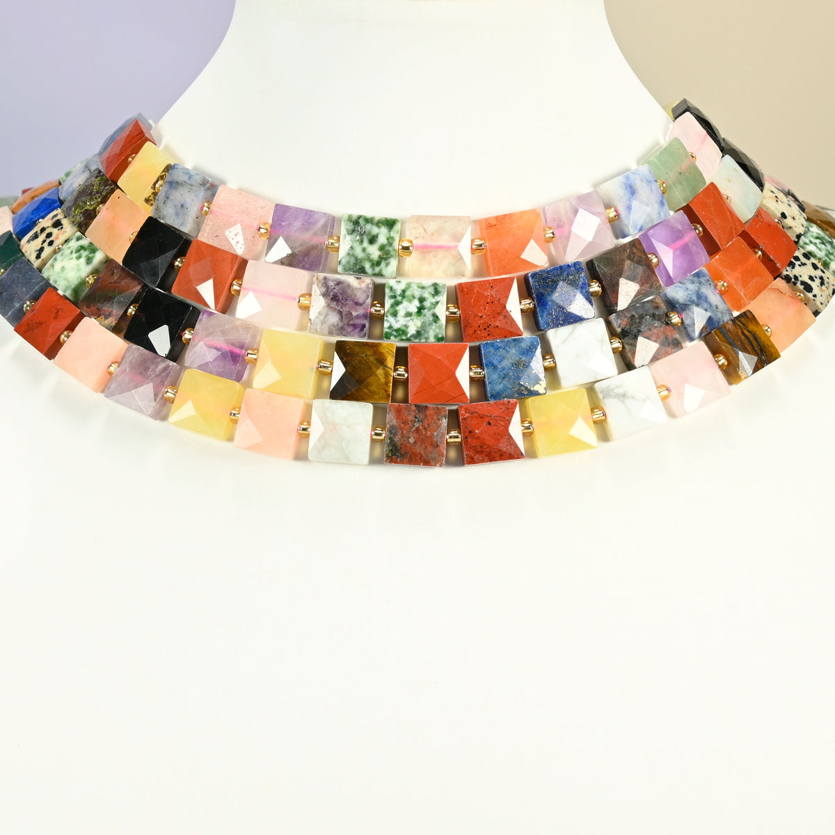Assorted gemstone faceted flat square strands arranged as a layered collar on a white display bust, multicolor beads across the neck