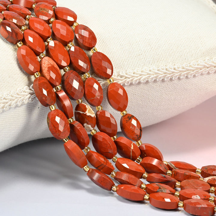 Flower red jasper faceted flat oval beads 9x14mm with small gold seed bead spacers, several strands draped over a white cushion