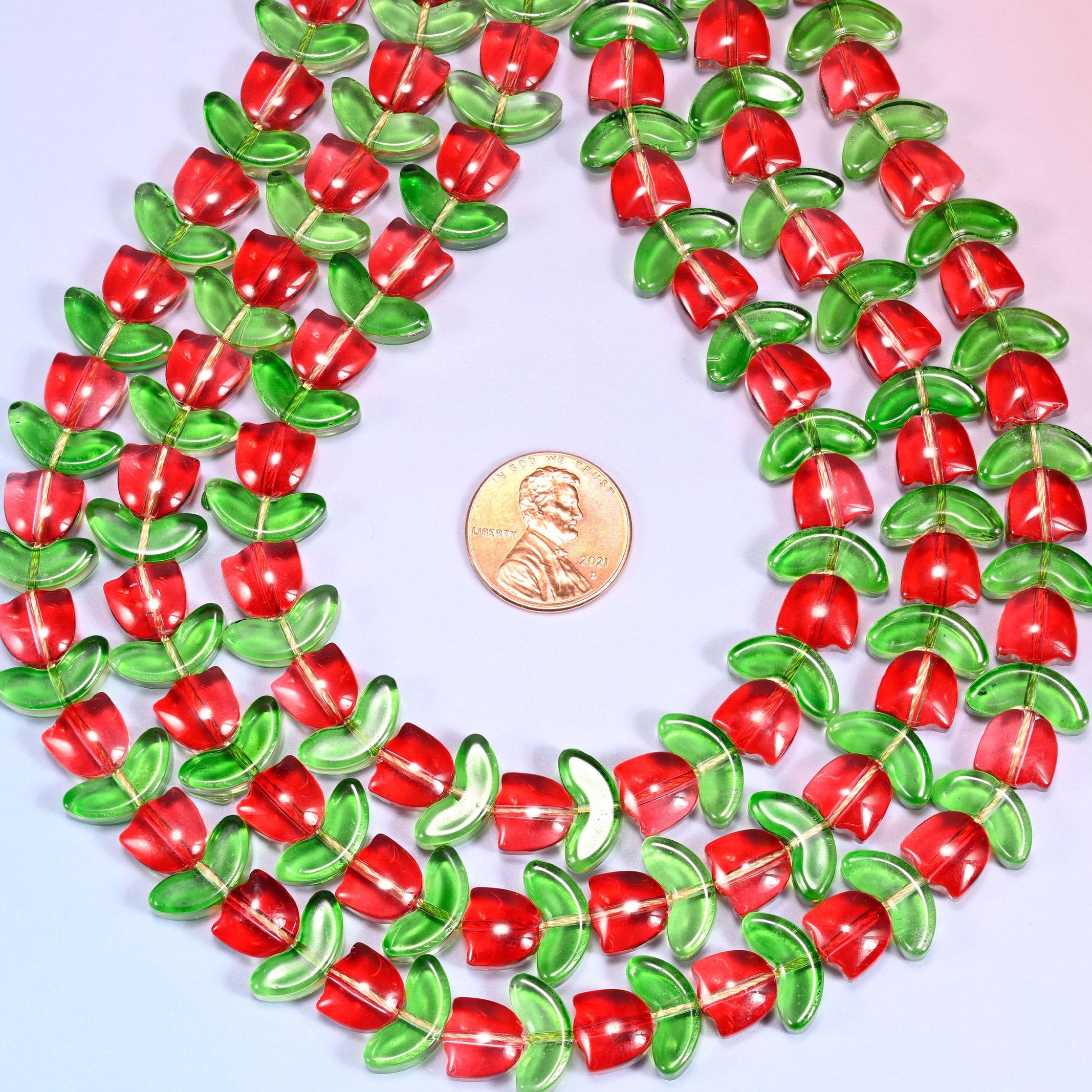 Circular coil of tulip and leaf glass bead strands on a lavender background with a penny in the center for size comparison.