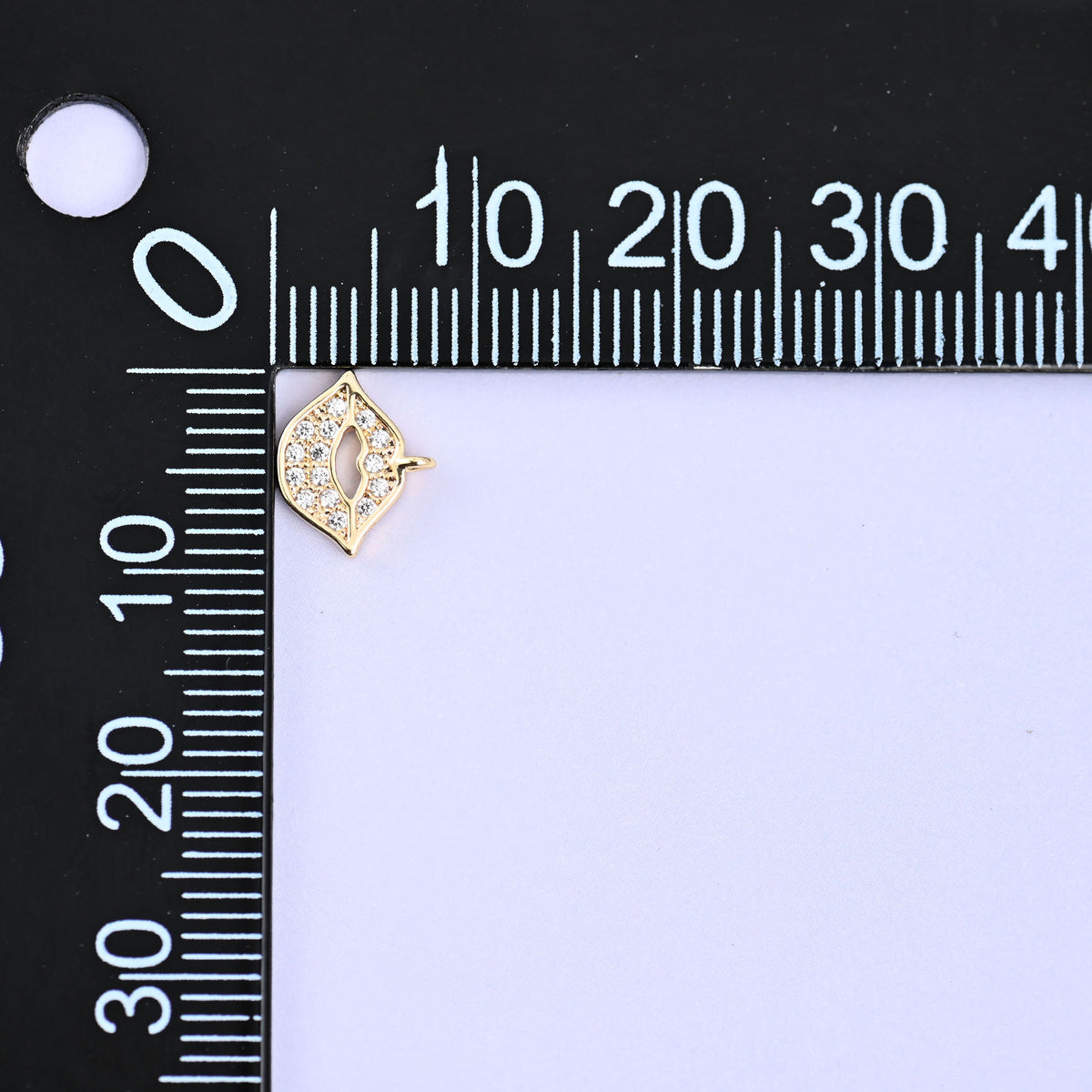 Small gold charms, one lip charm at the corner of a millimetre ruler showing the size