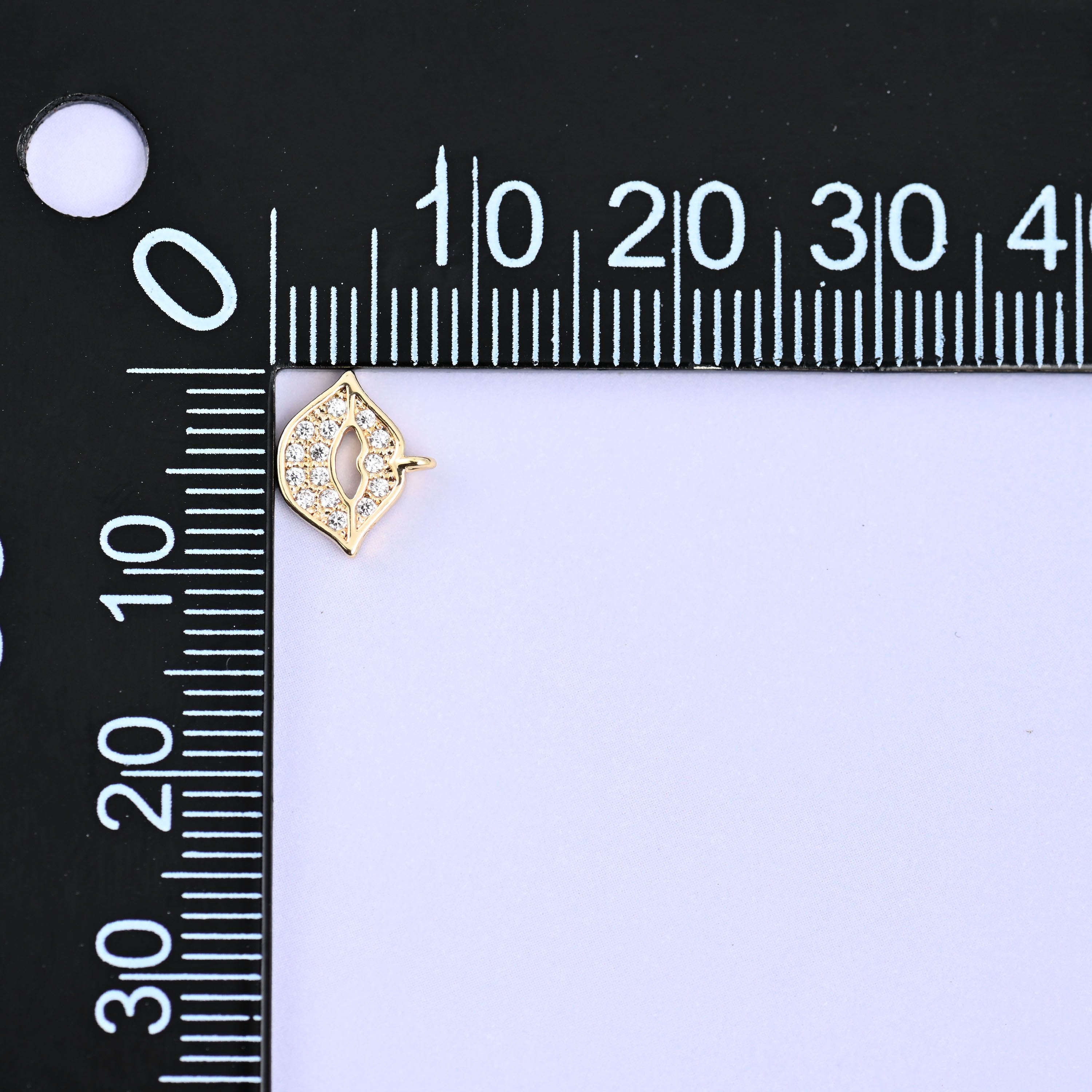 Small gold charms, one lip charm at the corner of a millimetre ruler showing the size
