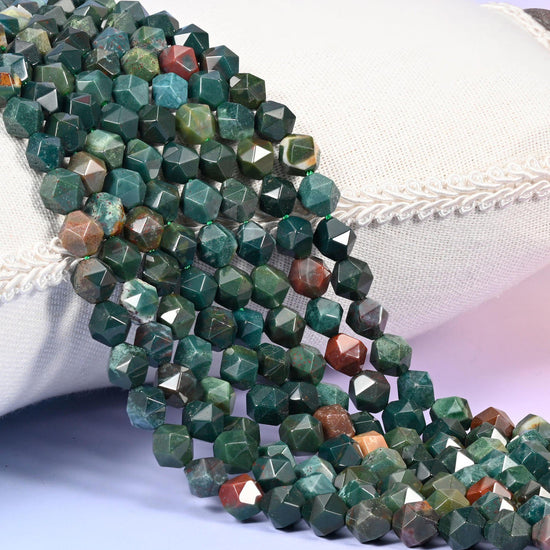 Indian Bloodstone diamond star cut beads, strands laid over white fabric, dark green stone with rust and red-brown beads mixed through