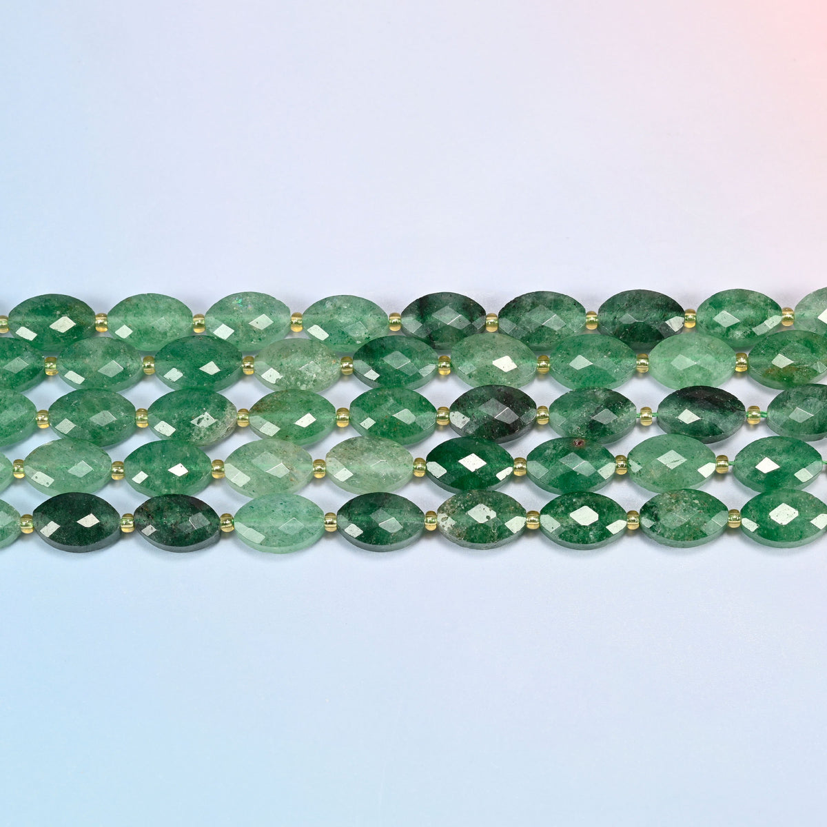 Several strands of green strawberry quartz faceted flat oval beads laid in straight rows with gold seed bead spacers