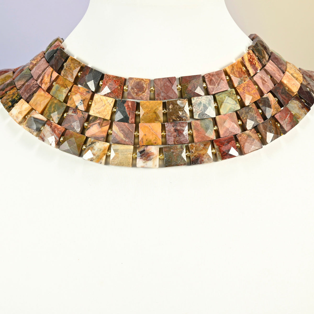 Natural red howlite faceted flat square strands arranged as a layered collar on a white display bust, red, green and tan beads across the neck