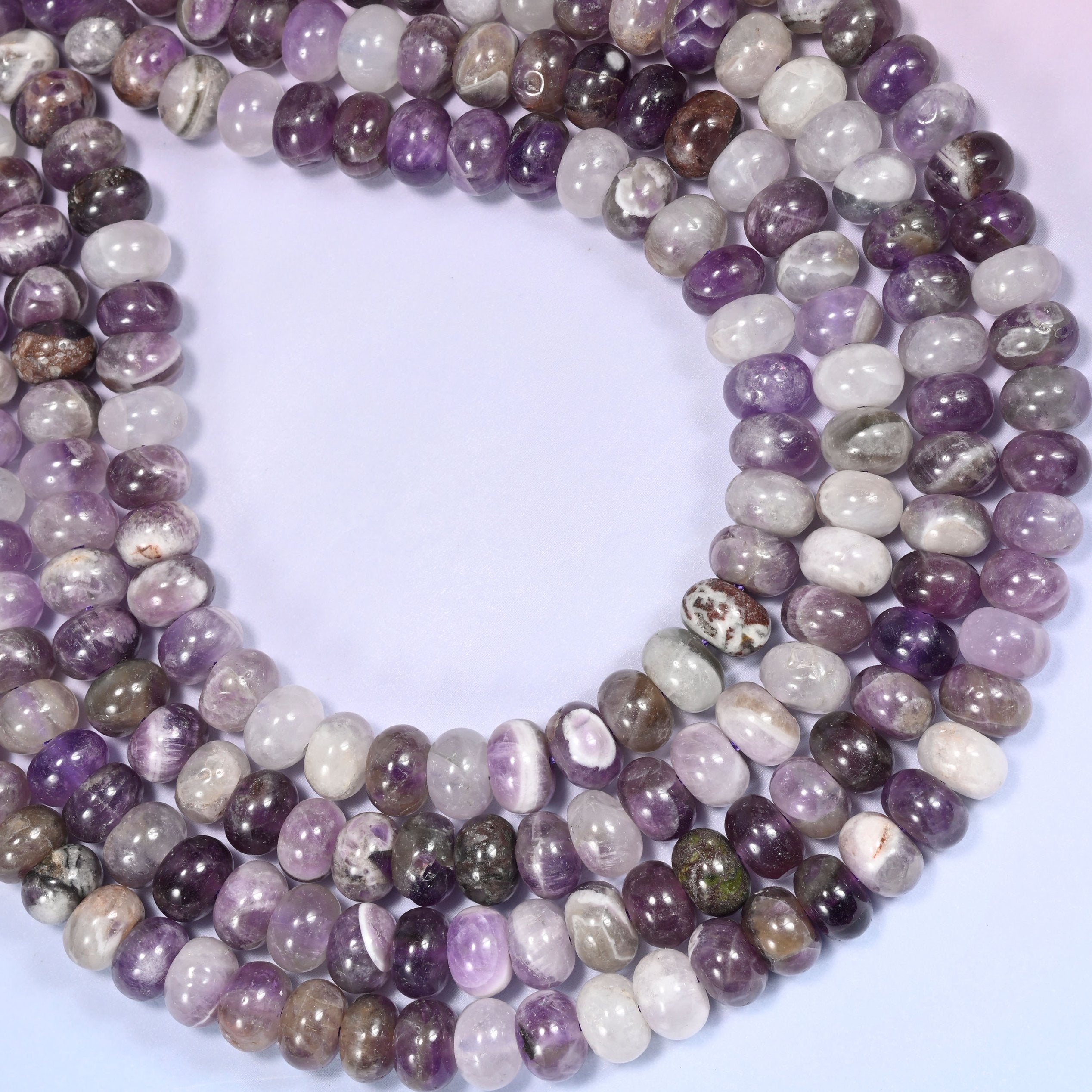 Circular coil of Amethyst bead strands on a lavender background with a penny in the center for size comparison.