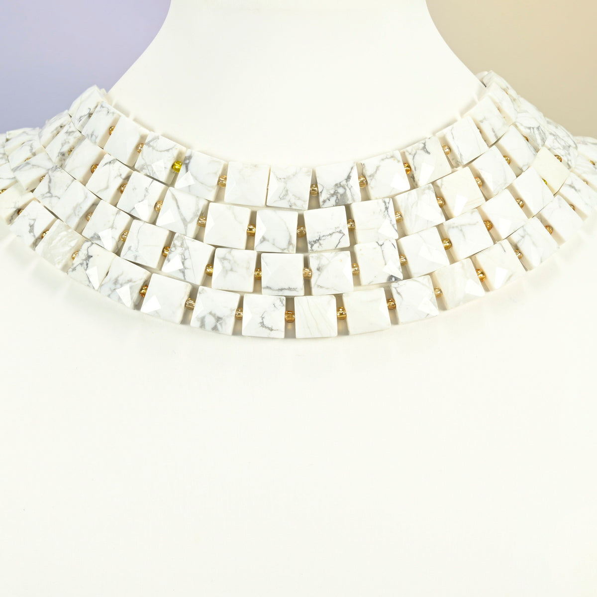 White howlite faceted flat square strands arranged as a layered collar on a white display bust, white beads across the neck