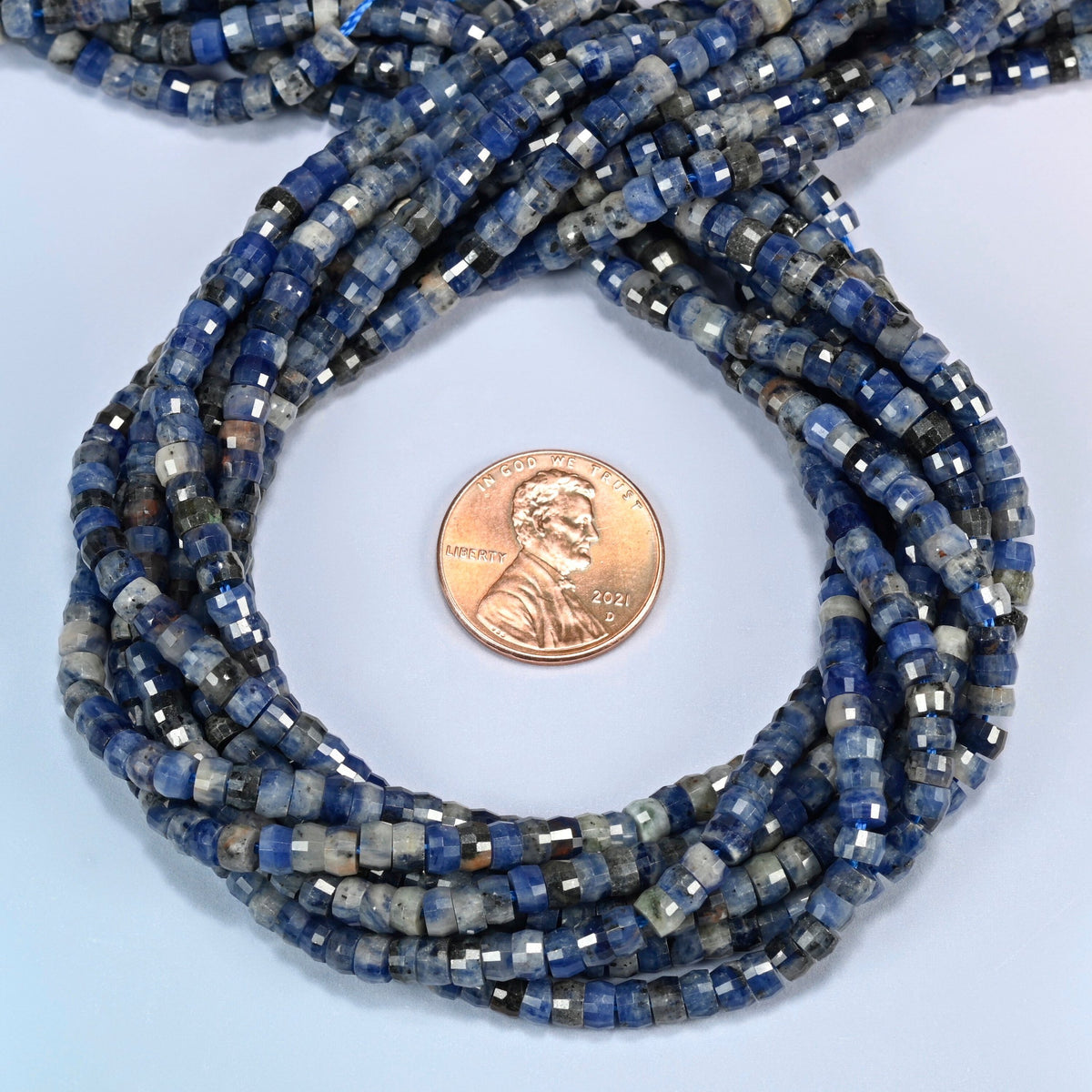 Sodalite faceted heishi disc beads 2x4mm coiled in a loop around a US penny for scale, close-up of the faceted disc shape