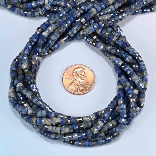 Sodalite faceted heishi disc beads 2x4mm coiled in a loop around a US penny for scale, close-up of the faceted disc shape