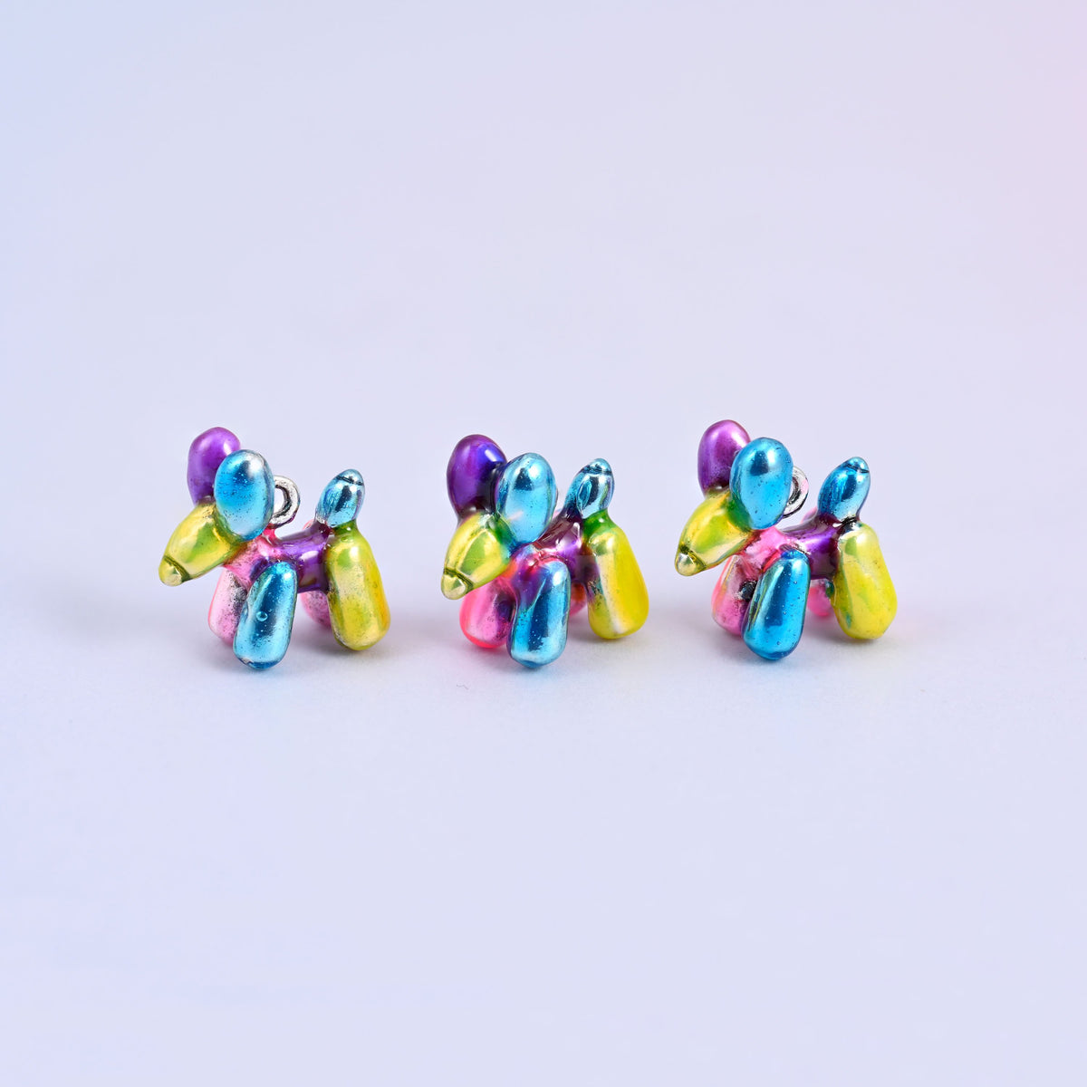 Three balloon dog charms in a row, metallic enamel in blue, purple, pink and yellow on 18K white gold plated brass.