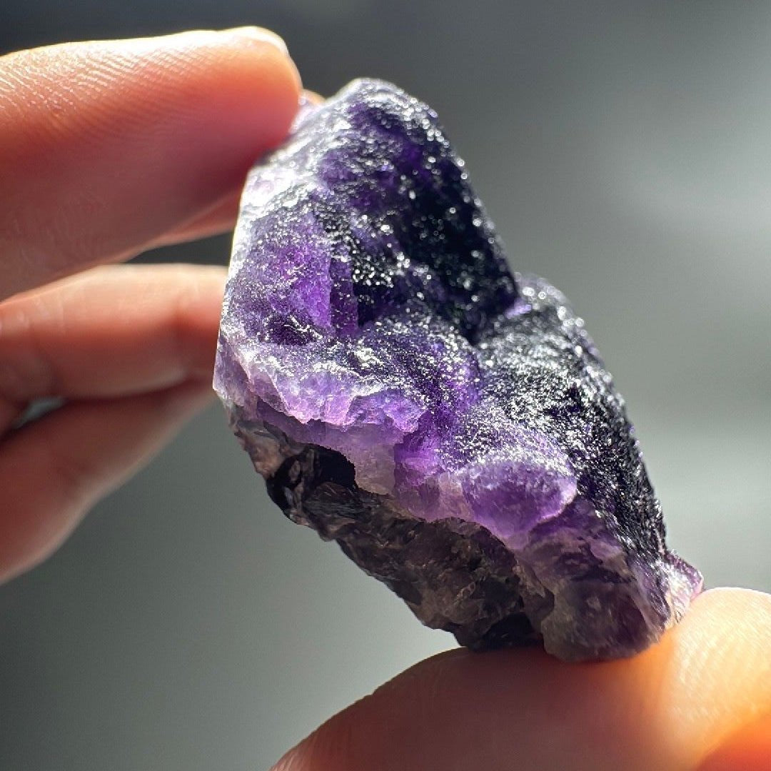 Hand holding the purple fluorite specimen showing vivid violet crystal zones.
