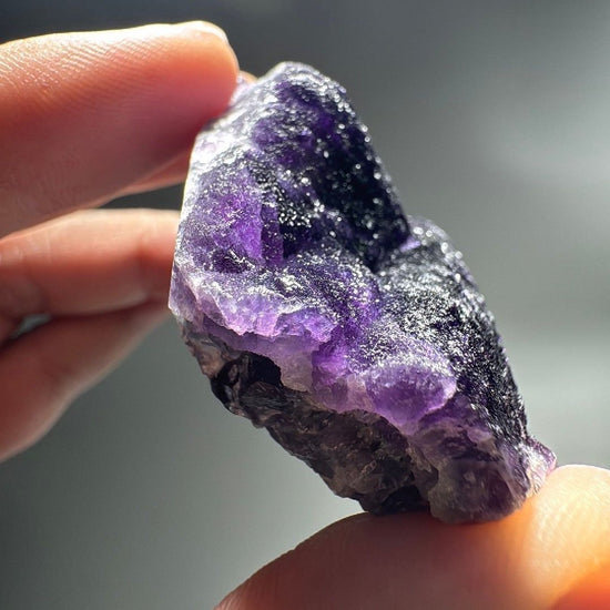 Hand holding the purple fluorite specimen showing vivid violet crystal zones.