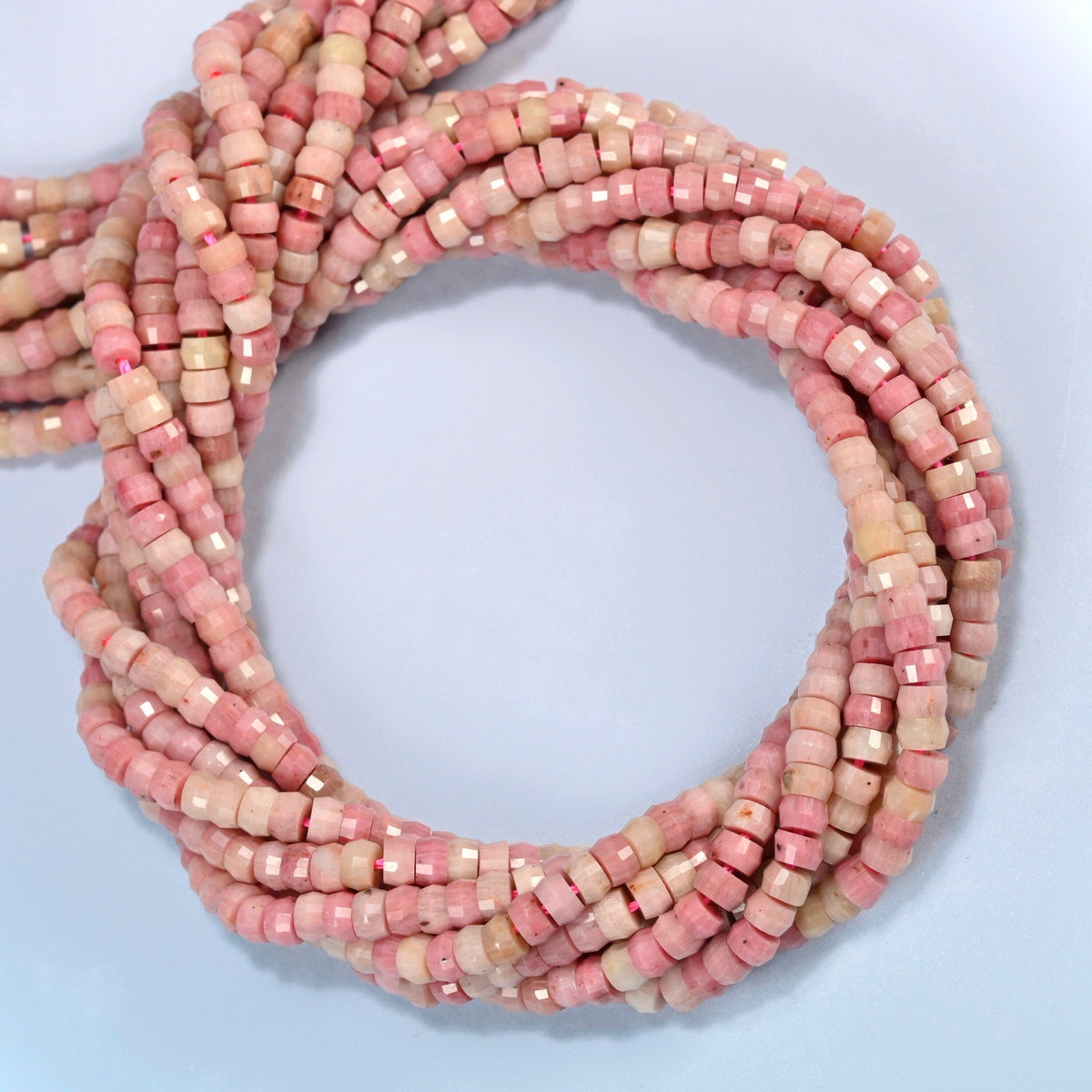 Pink rhodonite faceted heishi disc beads coiled into overlapping loops, whole strands of soft pink stone