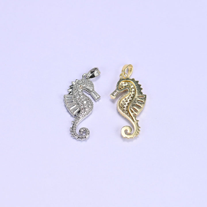Silver sea horse zirconia charm beside a gold one turned to its reverse, contrasting the paved face with the textured plain back.