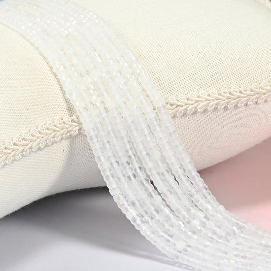 Clear quartz faceted heishi disc beads 2x4mm, several strands draped over a white cushion