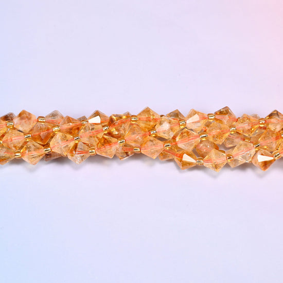 Citrine bicone beads shown as a single strand laid straight across, some beads paler and clearer, others a deeper orange.