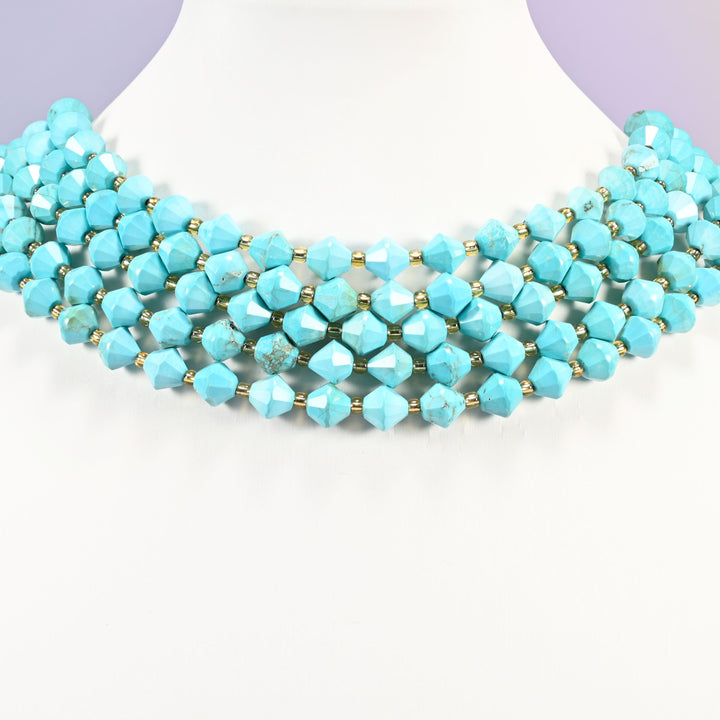 Dyed light blue howlite faceted bicone beads on a white neck display, five strands around the bust.
