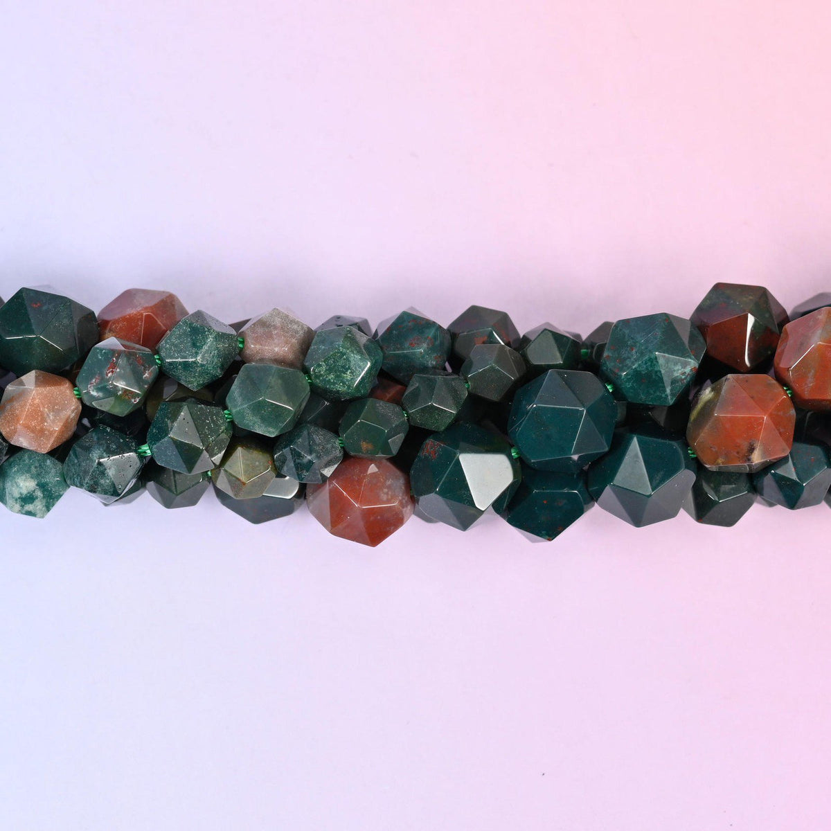 Indian Bloodstone faceted beads close up in a single row, flat triangular star cut planes over green and red-brown patterning