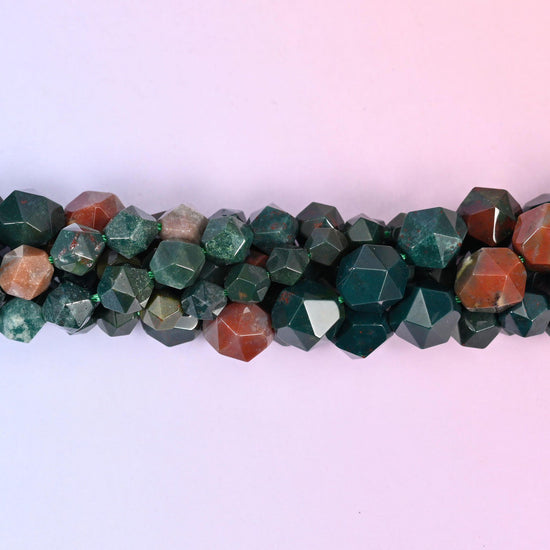 Indian Bloodstone faceted beads close up in a single row, flat triangular star cut planes over green and red-brown patterning