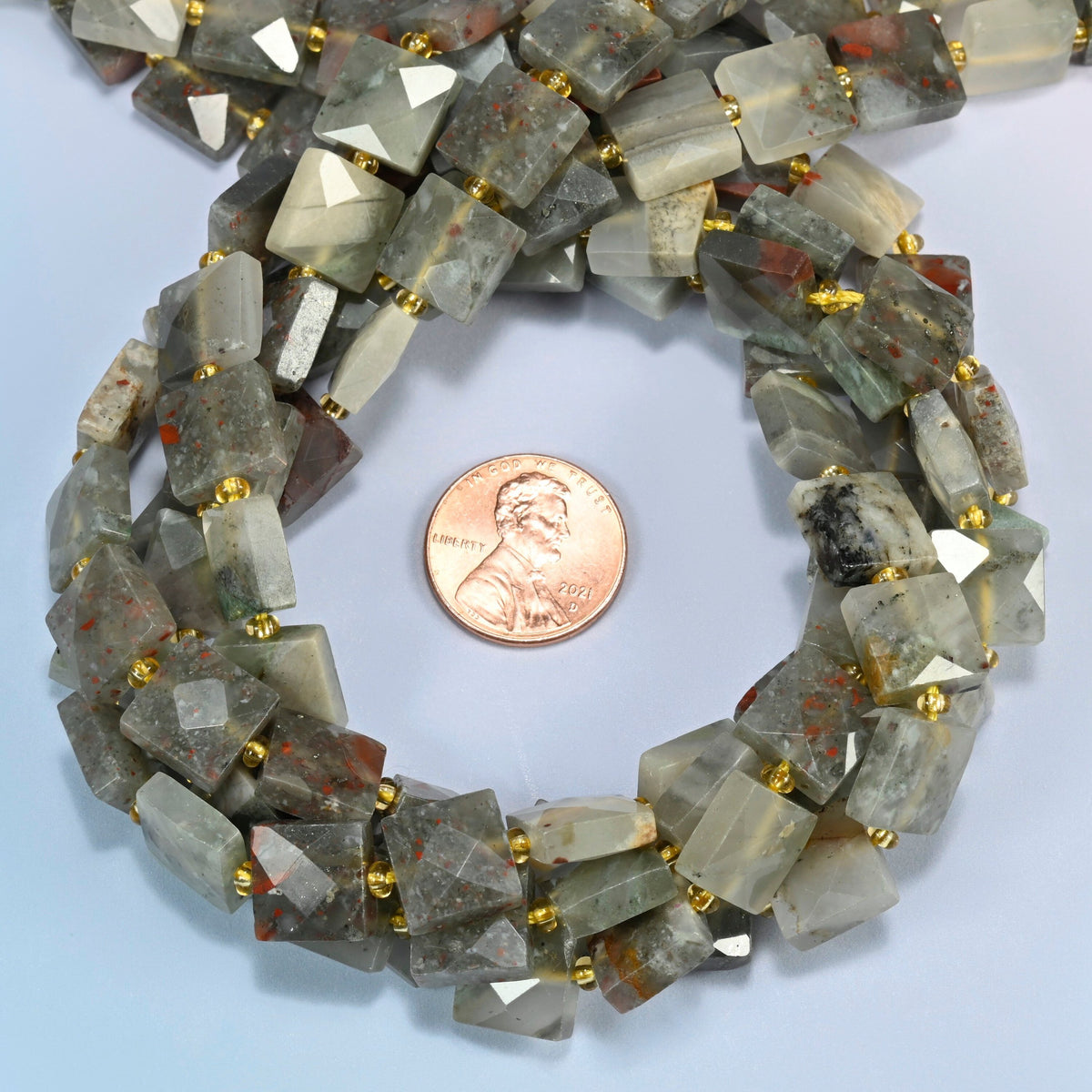 Natural African bloodstone faceted flat square beads 10x10mm coiled in a loop around a US penny for scale, close-up of the faceted flat square shape