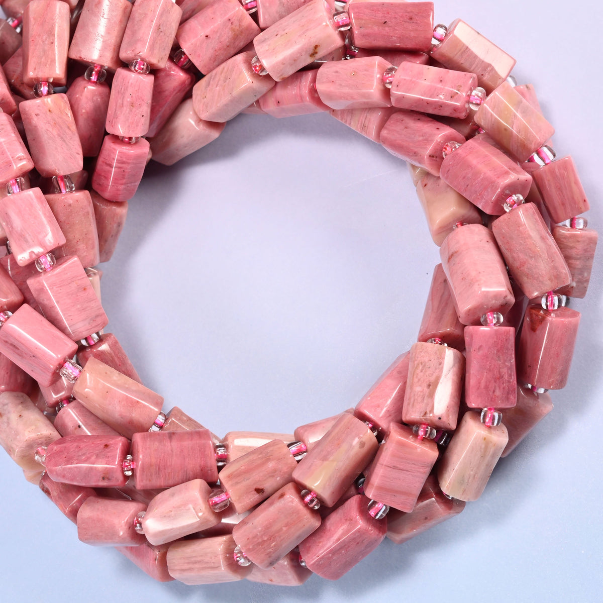 Pink Rhodonite faceted tube beads coiled into a ring, colour running from deeper rose to near cream from bead to bead