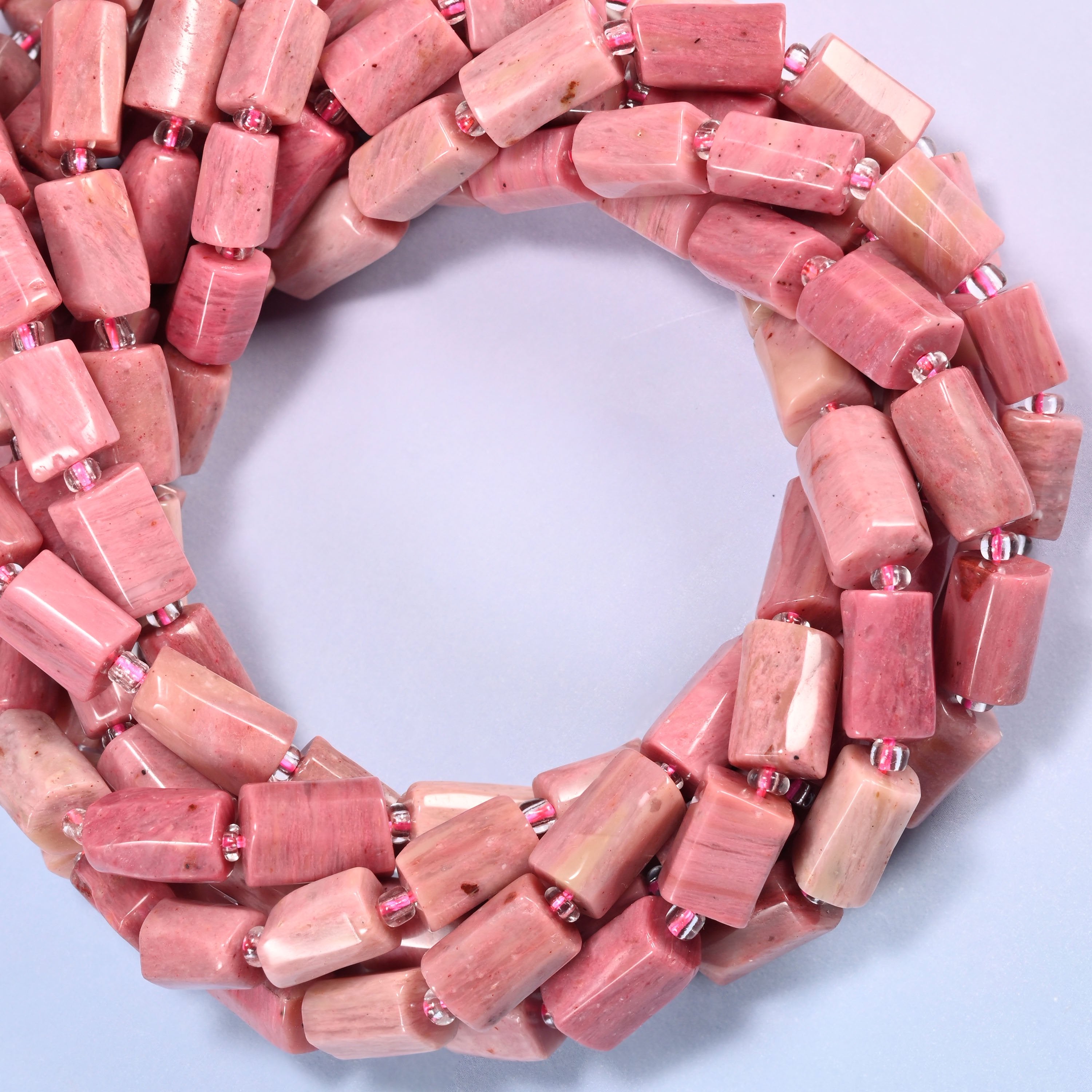 Pink Rhodonite faceted tube beads coiled into a ring, colour running from deeper rose to near cream from bead to bead