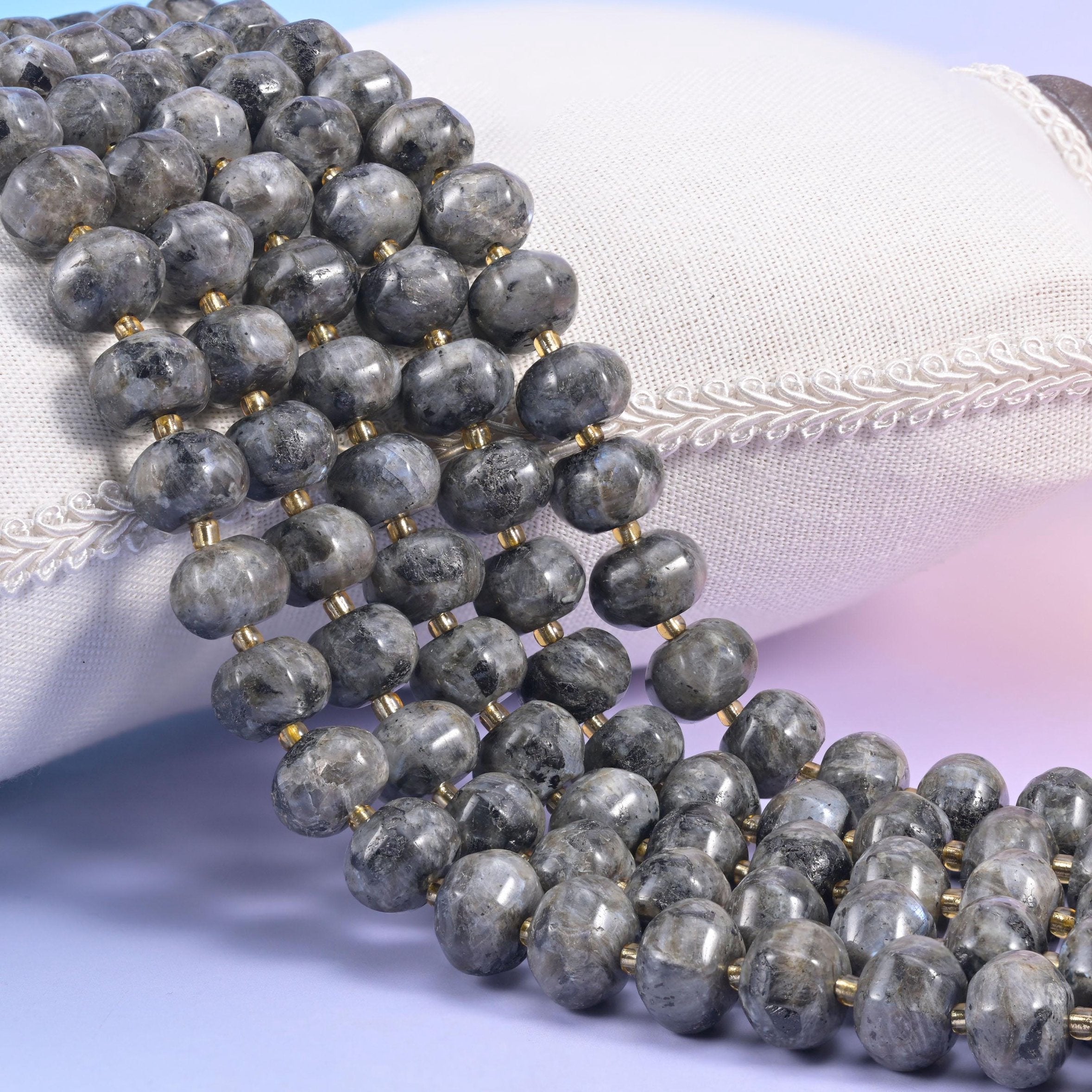 Black labradorite pumpkin rondelle strands on a cream cushion, ribbed grey beads with gold spacers