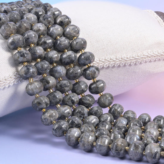 Black labradorite pumpkin rondelle strands on a cream cushion, ribbed grey beads with gold spacers