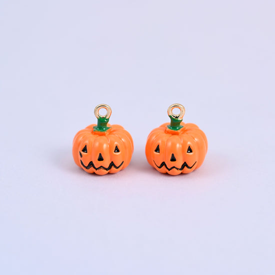 Two enamel pumpkin charms side by side, both showing the black jack o lantern face on the orange enamel body.
