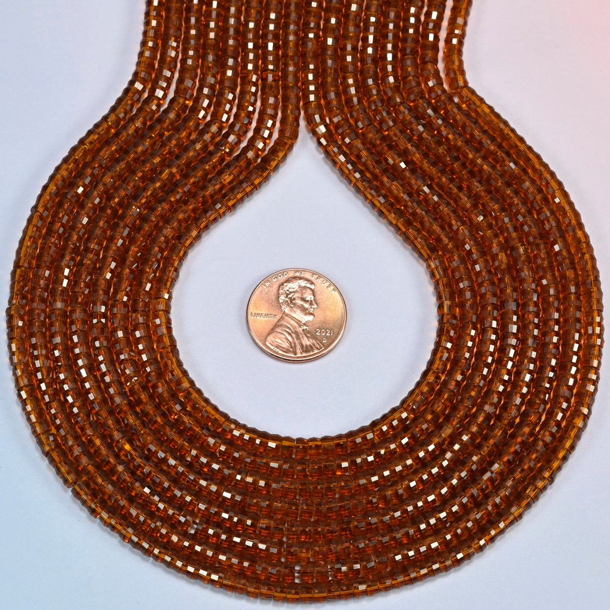 Brown glass faceted heishi disc strands formed into a teardrop loop around a US penny for scale
