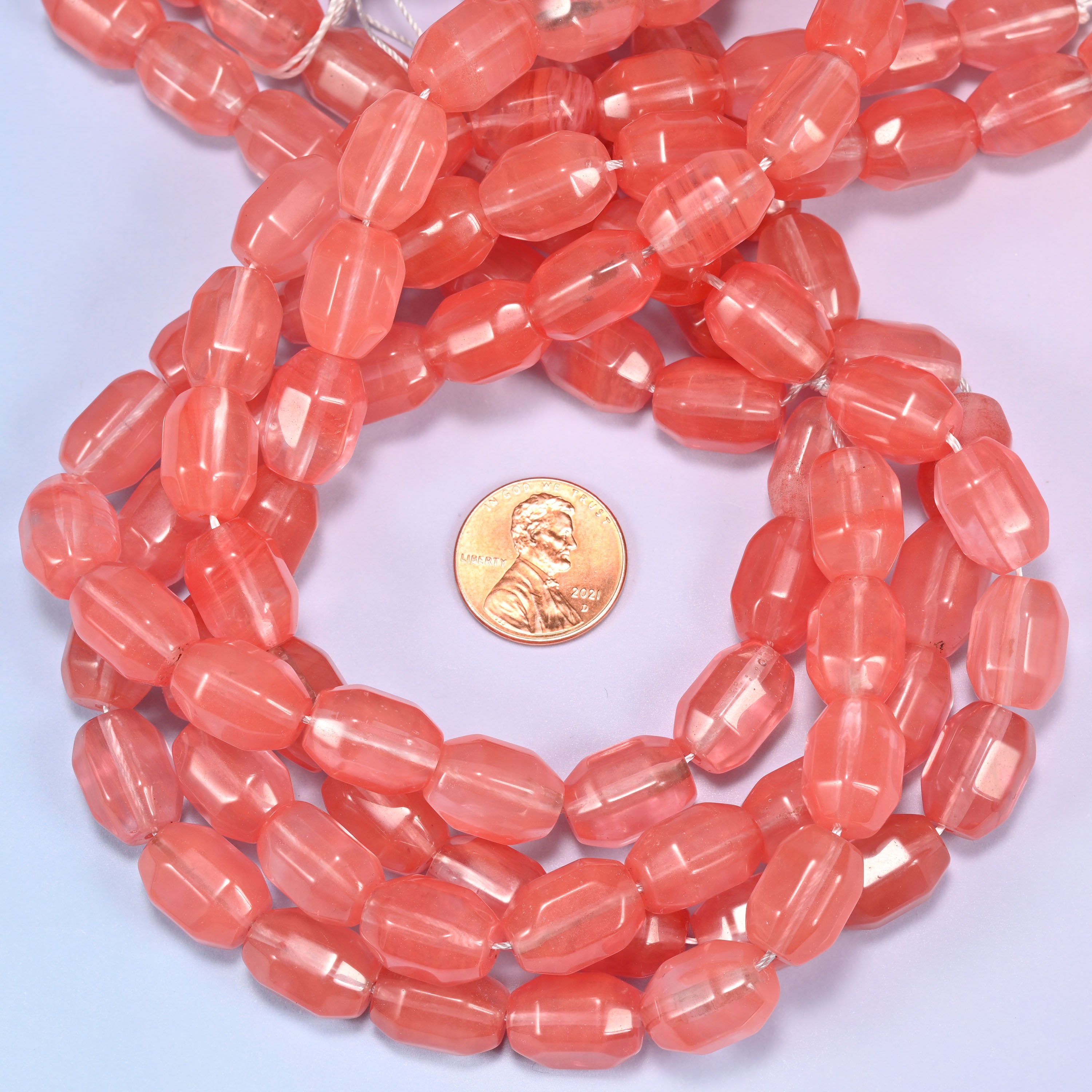 Close-up circular coil of faceted glass barrel bead strands with a penny in the center for size comparison.