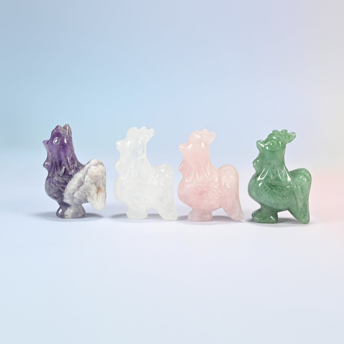 Four 2 inch rooster crystal carvings side by side in natural amethyst, clear quartz, rose quartz and green aventurine