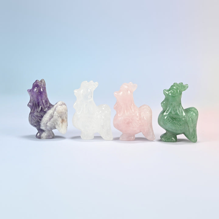 Four 2 inch rooster crystal carvings side by side in natural amethyst, clear quartz, rose quartz and green aventurine