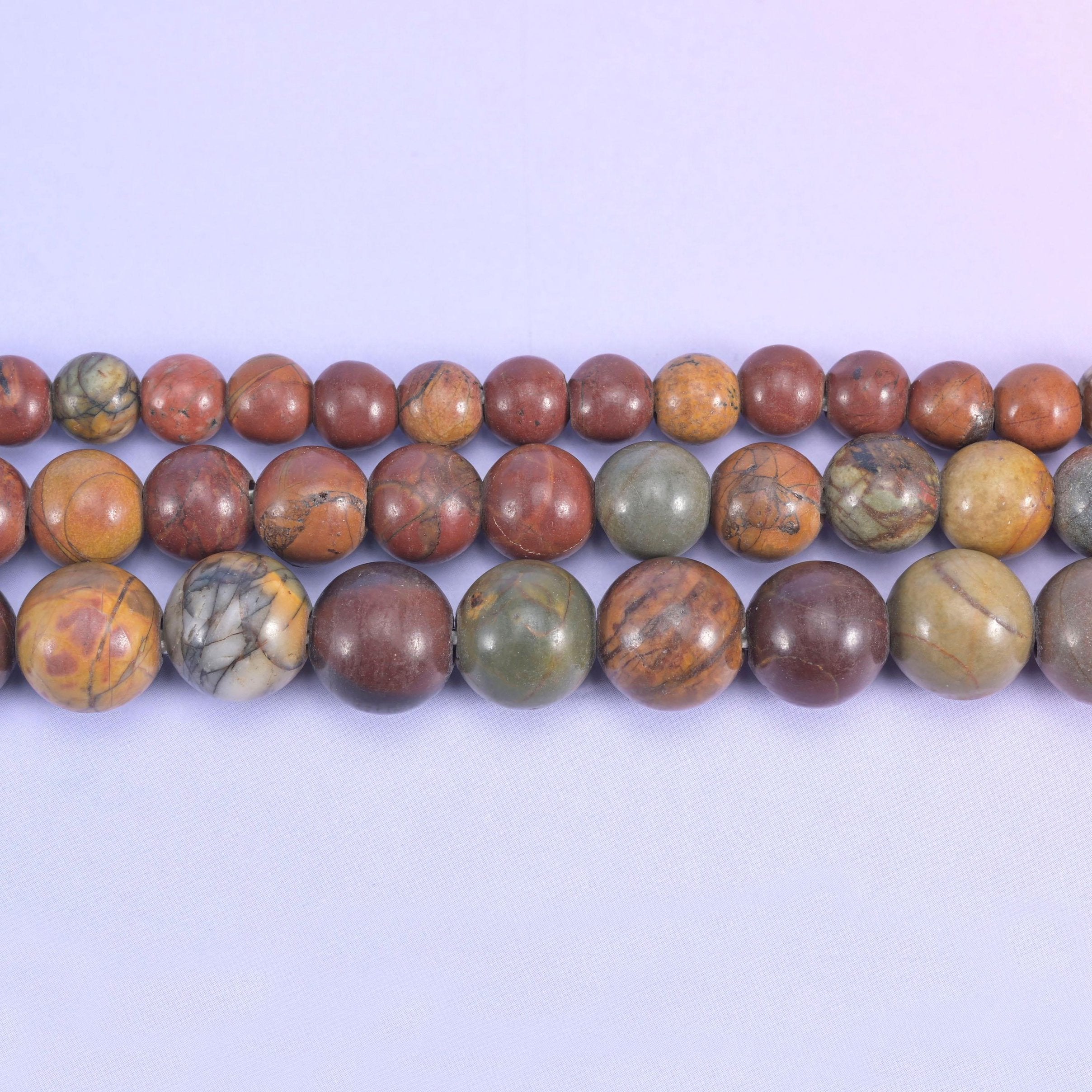 Brick red and terracotta rounds marbled with tan, cream and olive-grey, closer to a desert jasper than a plain red stone — and drilled 2.0-2.5mm so leather, thick cord and elastic go straight through.