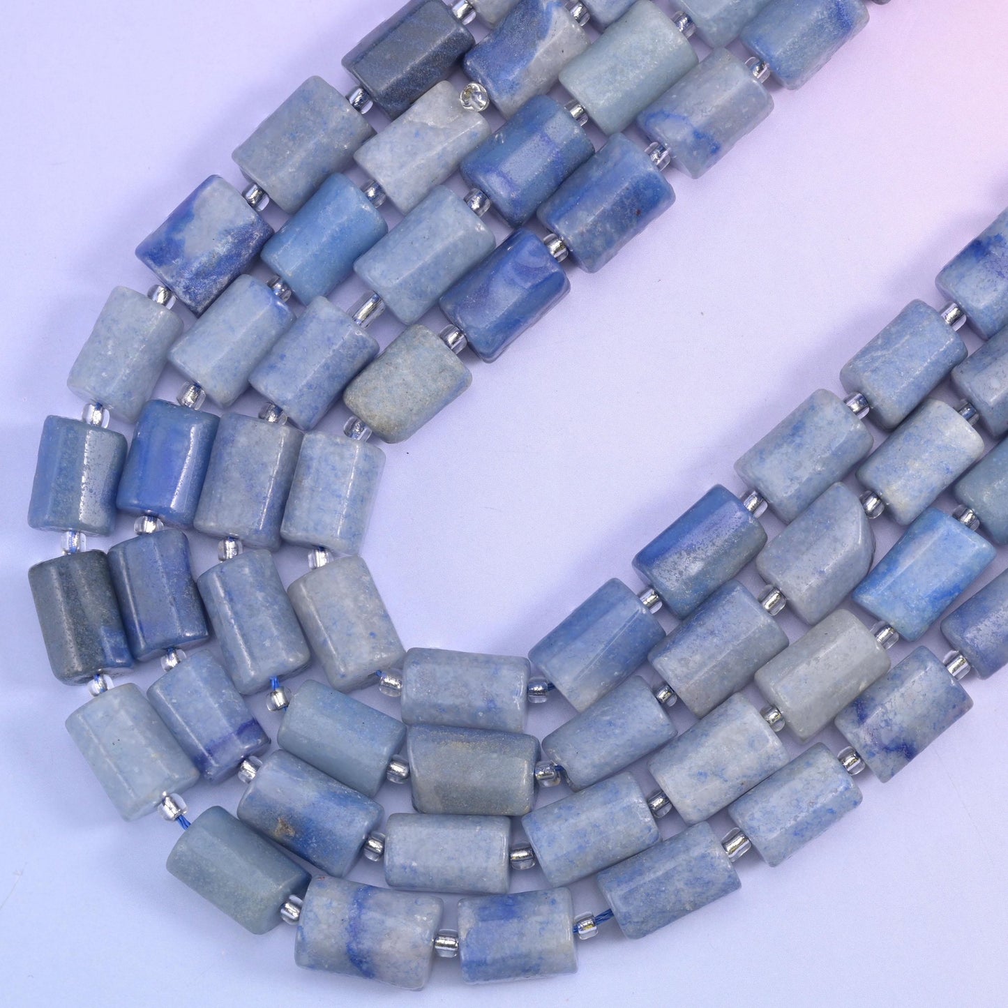 Faceted aventurine tube strands curving into a wide V on a pale lavender background