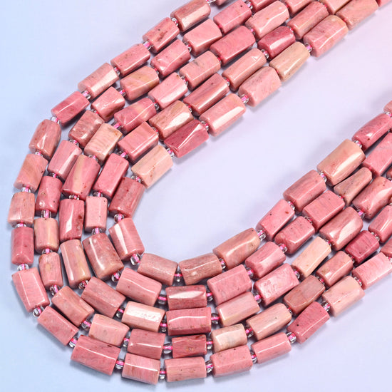 Pink Rhodonite faceted tube beads curving in a wide U across the frame, dusty rose shading into warm salmon and cream