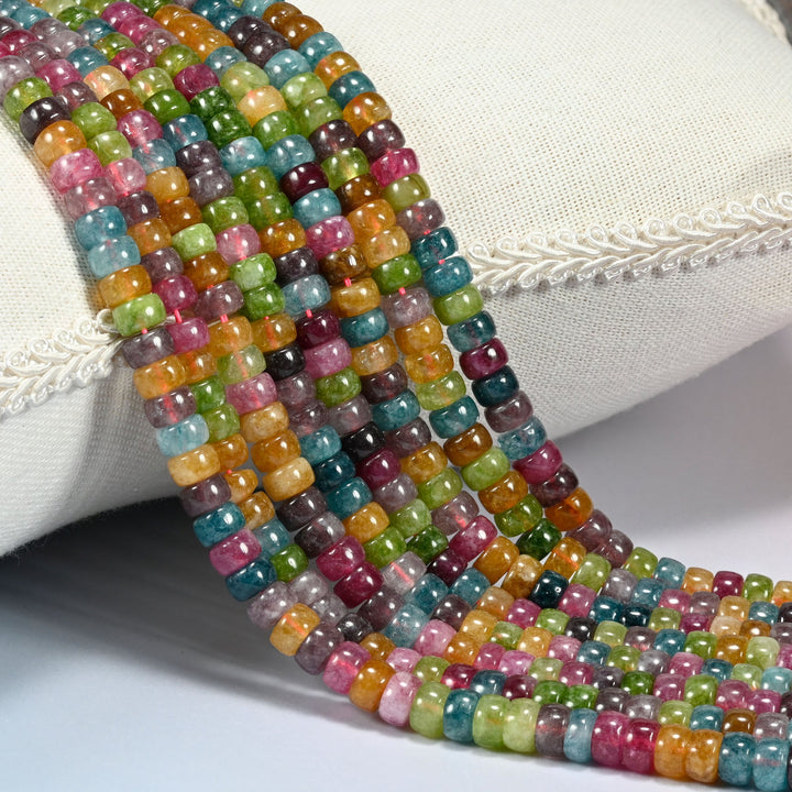 Tourmaline Color Dyed Jade round disc beads 3x6mm draped over a cream cushion, rose pink, teal blue, apple green and golden yellow mixed bead to bead along every strand