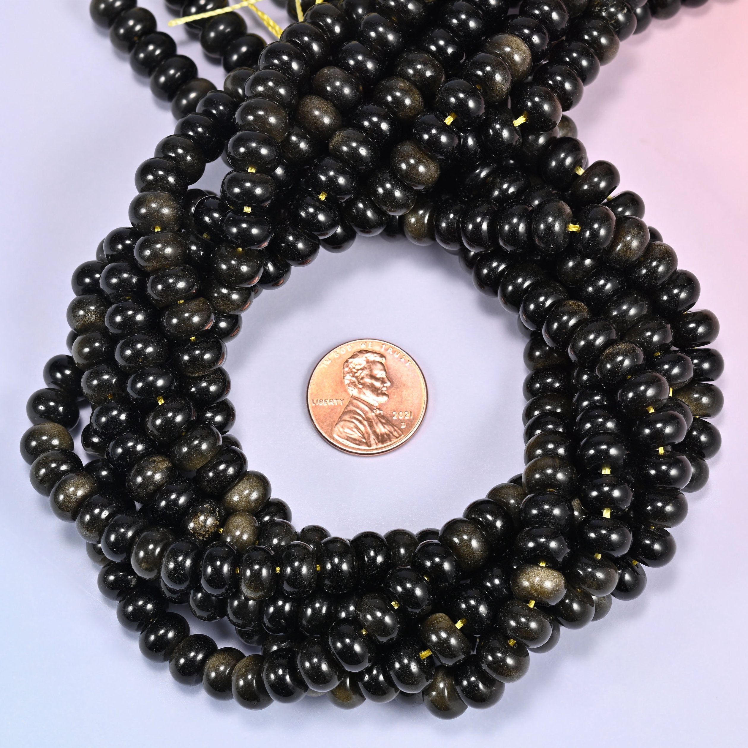 Multiple strands of Gold Obsidian beads gathered together on a lavender surface, loose ends visible.