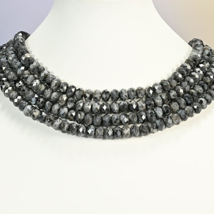 Black labradorite faceted rondelle strands arranged as a layered collar on a white display bust, gray speckled beads across the neck