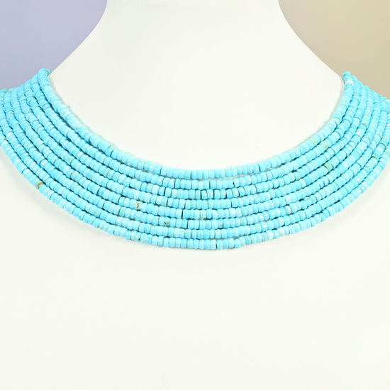 Dyed blue howlite faceted heishi disc strands arranged as a layered collar on a white display bust, turquoise blue beads across the neck
