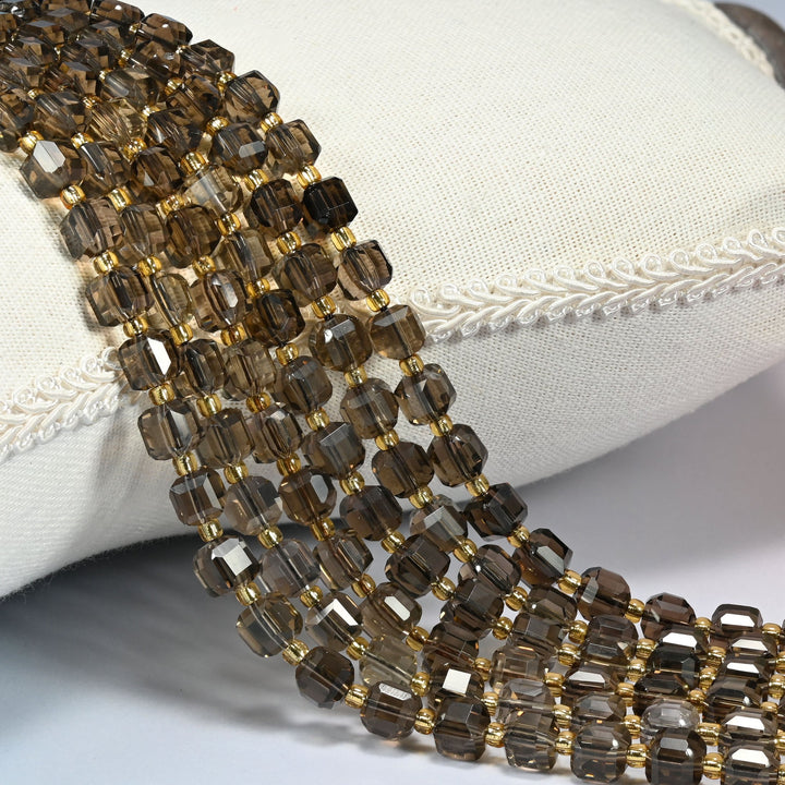 Smoky quartz faceted cube beads with gold glass seed bead spacers draped over a white linen cushion.