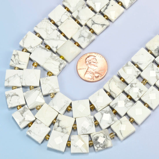 Close view of white howlite faceted flat square strands curving beside a US penny for scale