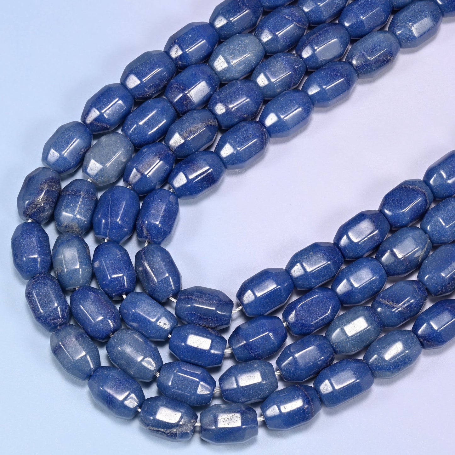 Close-up of a circular coil of blue faceted Aventurine barrel beads on a light blue background.