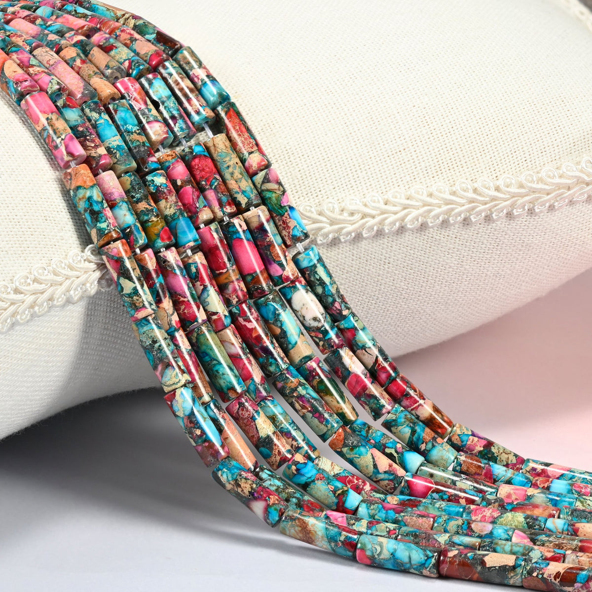 Dyed sea sediment jasper tube beads 13x4mm, several strands of turquoise, pink and brown tubes draped over a white cushion