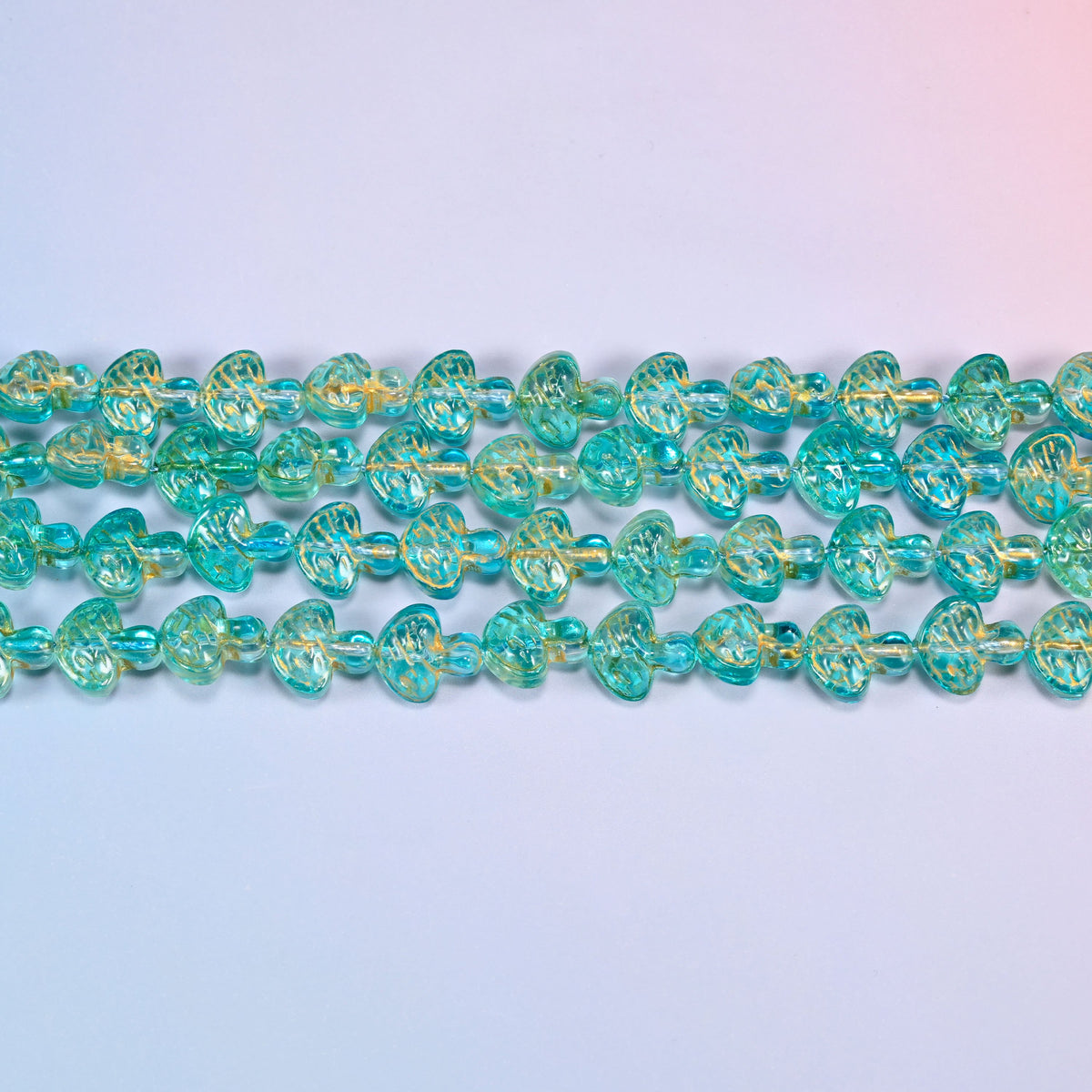 Close-up of 13x12mm aqua gold flat mushroom glass beads in four horizontal rows, showing the molded gill lines.