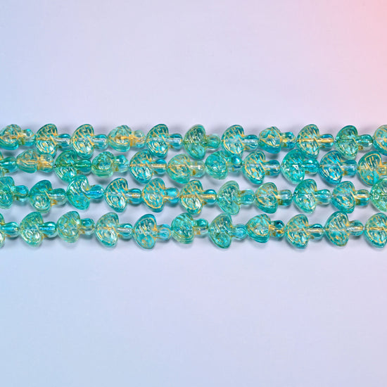 Close-up of 13x12mm aqua gold flat mushroom glass beads in four horizontal rows, showing the molded gill lines.